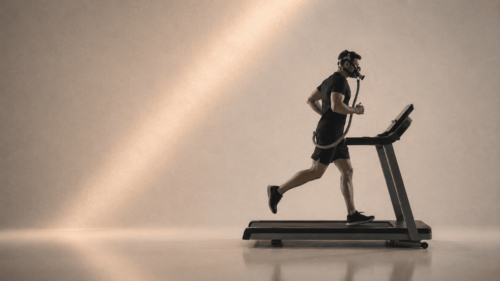 Side-profile of an athlete running on a treadmill wearing a VO2 metabolic analyzer mask, lit by warm raking light.